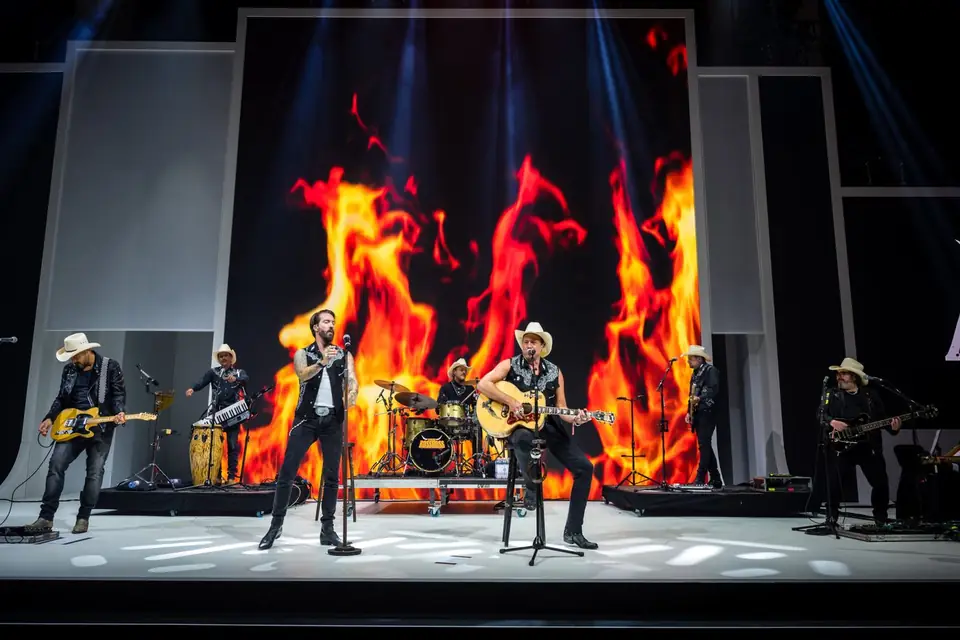 A band on stage in front of a wall of projected flame